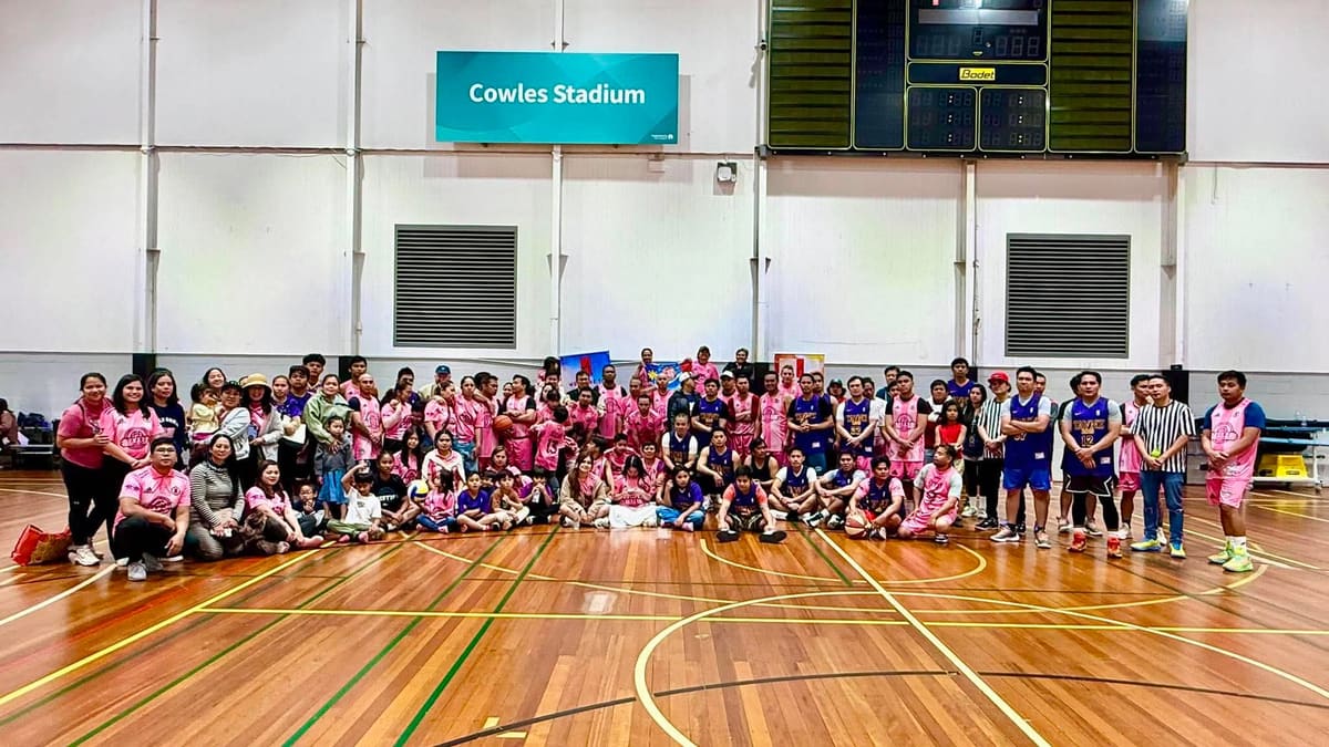 A large gathering of players, families, and children posing together on an indoor basketball court