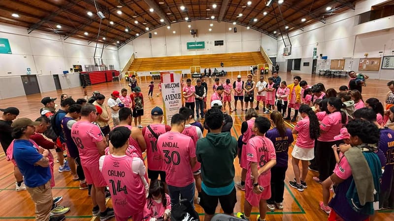 People standing in a circle on a basketball court with heads bowed in prayer